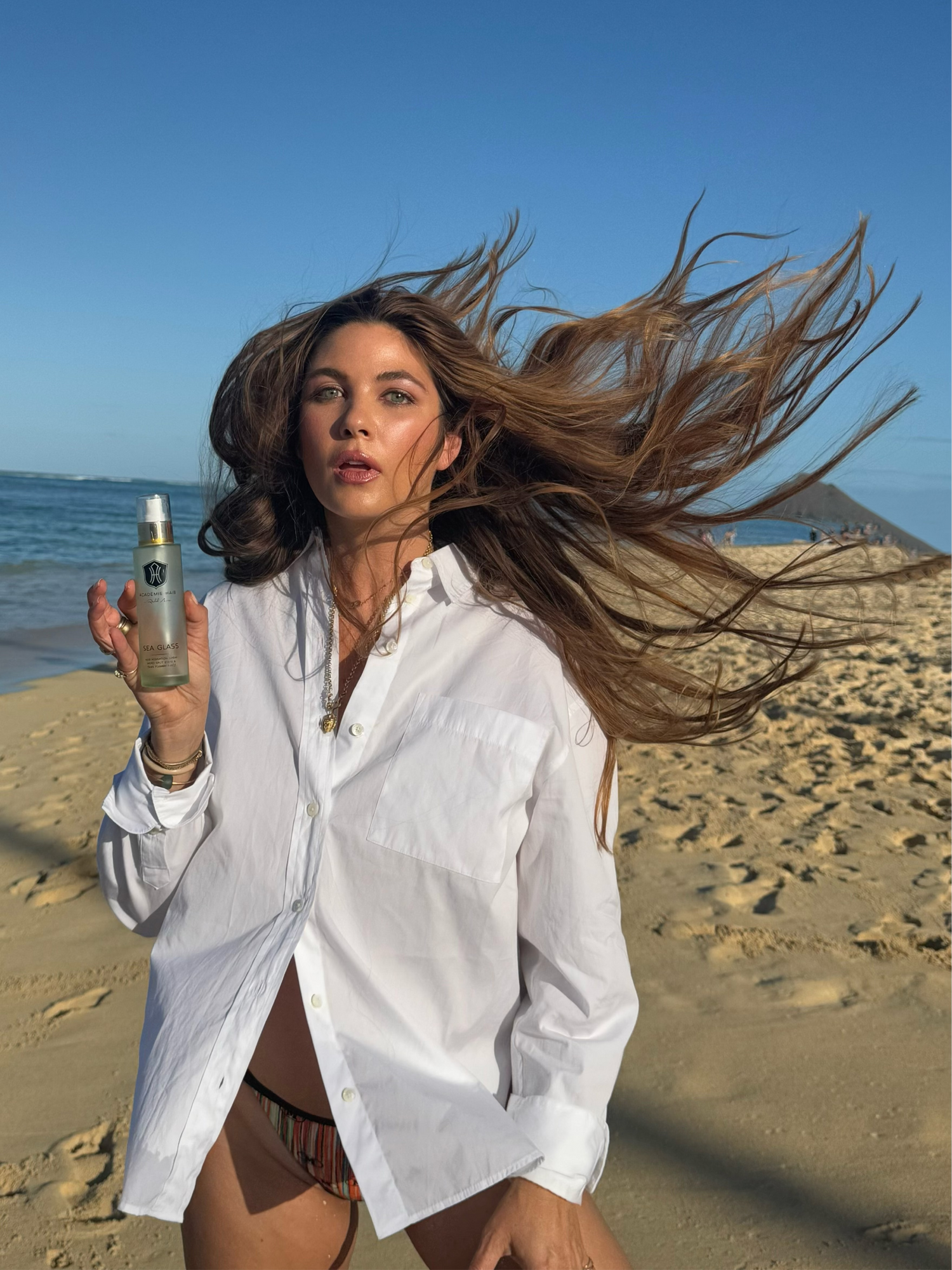 Rachel on windy beach holding Sea Glass bottle, with the ocean and clear sky in the background